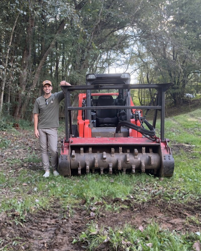 James Barlow standing beside his Kubota track loader and forestry mulching head on ground he has just cleared